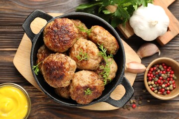 Tasty patties, dill in frying pan, parsley, mustard and peppercorns on wooden table, flat lay
