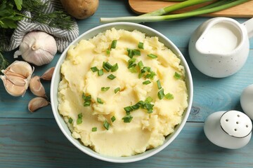 Delicious mashed potato with green onions served on light blue wooden table, flat lay