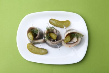 Delicious herring rolls with pickles and dill on light green table, top view