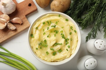 Tasty mashed potato with green onion in bowl, dill, spices and raw vegetables on white table, flat lay