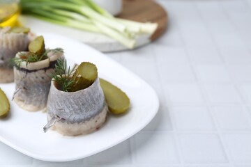 Delicious herring rolls with pickles and dill on light tiled table, closeup. Space for text