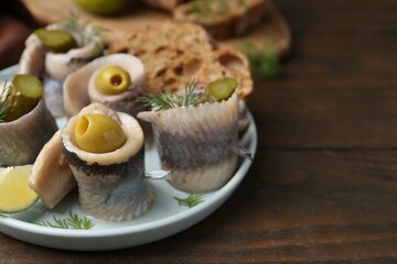 Delicious herring rolls with olives, pickles and dill on wooden table, closeup. Space for text