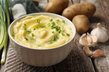 Tasty mashed potato with green onion in bowl and raw vegetables on wooden table, closeup