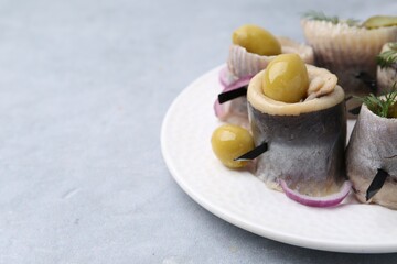 Delicious herring rolls with olives, pickles, dill and onion on gray table, closeup. Space for text