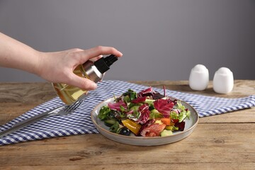 Woman with bottle of oil and salad at wooden table against grey background, closeup