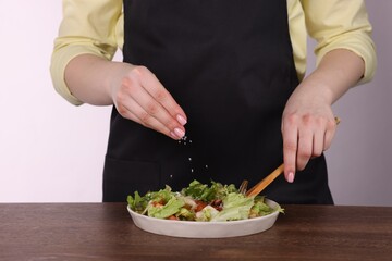 Woman salting tasty salad at wooden table against white background, closeup
