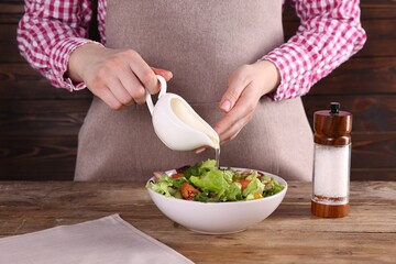Woman pouring oil onto tasty salad at wooden table, closeup