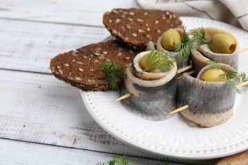 Delicious herring rolls with olives, dill and bread on white wooden table, closeup. Space for text