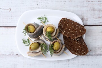 Delicious herring rolls with olives, dill and bread on white wooden table, top view