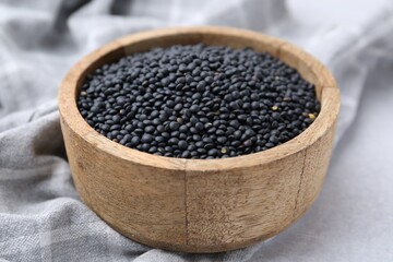 Black lentils in bowl on light table, closeup