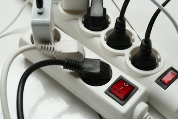 Extension power boards overloaded with plugs on wooden floor, closeup