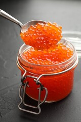 Taking tasty red caviar with spoon from glass jar on grey table, closeup