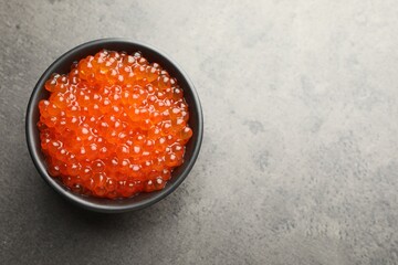 Tasty red caviar in bowl on grey table, top view. Space for text
