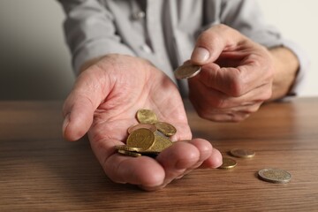 Fototapeta premium Senior man counting coins at wooden table, closeup. Financial problems