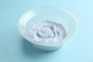 Bowl with hair bleaching powder on light blue background, closeup