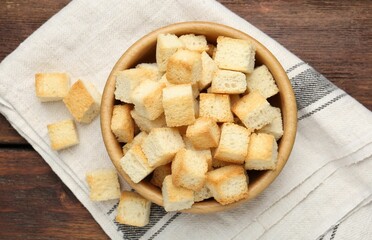 Delicious crispy croutons in bowl on wooden table, top view