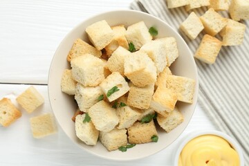 Delicious crispy croutons with parsley and sauce on white wooden table, flat lay