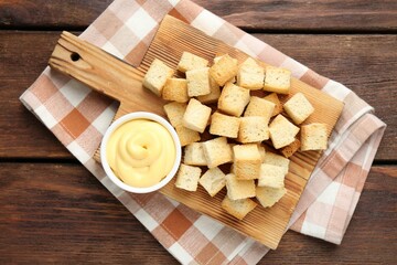 Delicious crispy croutons with sauce on wooden table, top view