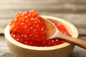 Taking red caviar with spoon from bowl at wooden table, closeup