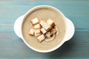 Delicious mushroom cream soup with croutons on blue wooden table, top view