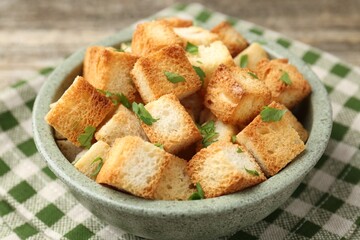 Tasty crispy croutons with cut parsley in bowl on table, closeup