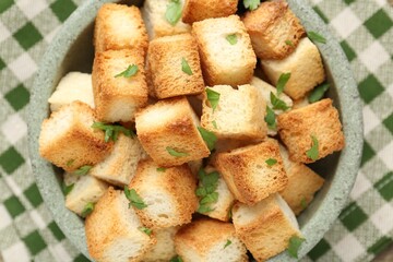 Tasty crispy croutons with cut parsley in bowl on table, top view