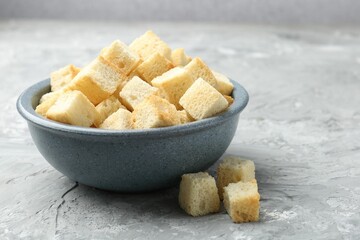 Tasty crispy croutons in bowl on grey textured table, closeup
