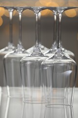 Upturned empty clean glasses on mirror surface against blurred background, closeup. Bokeh effect