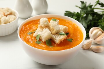 Delicious pumpkin cream soup with croutons, parsley and ingredients on light table, closeup