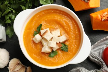 Tasty pumpkin cream soup with croutons and parsley in bowl among other products on dark textured...