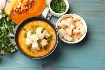 Tasty pumpkin cream soup with croutons and green onion in bowl on light blue wooden table, flat lay