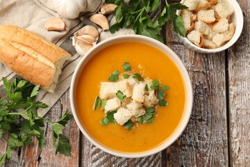 Tasty pumpkin cream soup with croutons and parsley in bowl on wooden table, flat lay