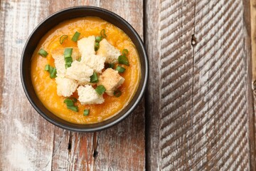 Tasty pumpkin cream soup with croutons and green onion in bowl on wooden table, top view. Space for text
