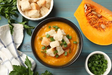 Tasty pumpkin cream soup with croutons, green onion and parsley on light blue wooden table, flat lay