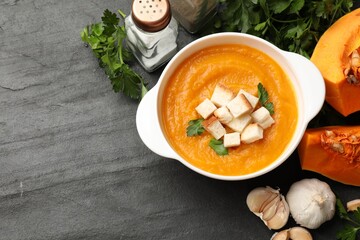 Tasty pumpkin cream soup with croutons and parsley in bowl among other products on dark textured...