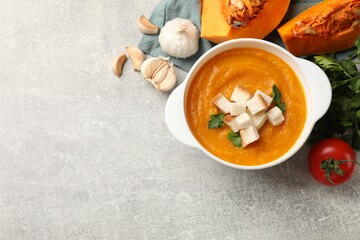 Tasty pumpkin cream soup with croutons and parsley in bowl among other products on grey textured...