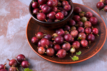 Red gooseberries on a clay plate and in a bowl on a gray table. Berry picking