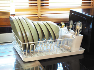 Dish drainer or dish rack with clean dinnerware on counter in kitchen.