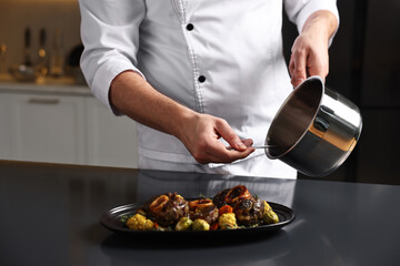 Professional chef adding sauce to delicious dish at table indoors, closeup