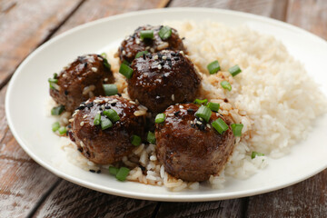 Delicious rice with meatballs, sauce and green onions on wooden table, closeup