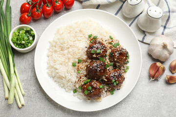 Delicious rice with meatballs, sauce and green onions on grey table, flat lay