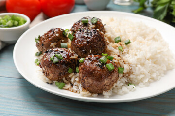 Delicious rice with meatballs, sauce and green onions on blue wooden table, closeup