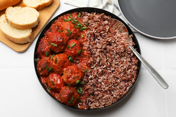 Tasty meatballs with sauce and brown rice on white tiled table, flat lay