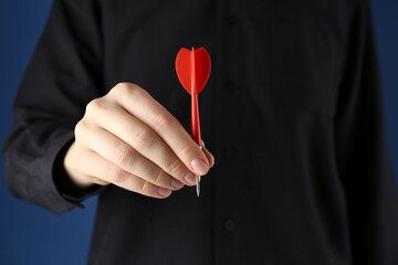 Woman holding dart on blue background, closeup
