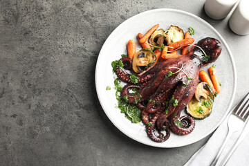 Roasted octopus served with vegetables and mushrooms on grey table, flat lay. Space for text