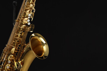 Fototapeta premium Jazz. One beautiful saxophone hanging from strap on black background, closeup. Space for text