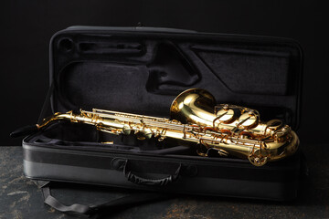 Naklejka premium Jazz. Golden saxophone in case on black textured table