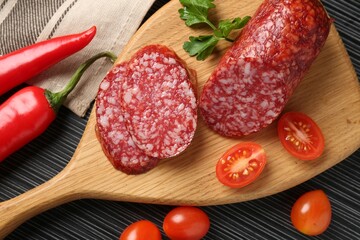 Cut smoked sausage, parsley, tomatoes and chili pepper on black wooden table, flat lay