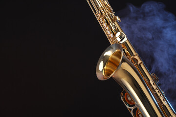 Golden saxophone on black background with smoke, closeup. Space for text