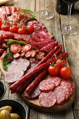 Different smoked sausages and other snacks served on wooden table, closeup
